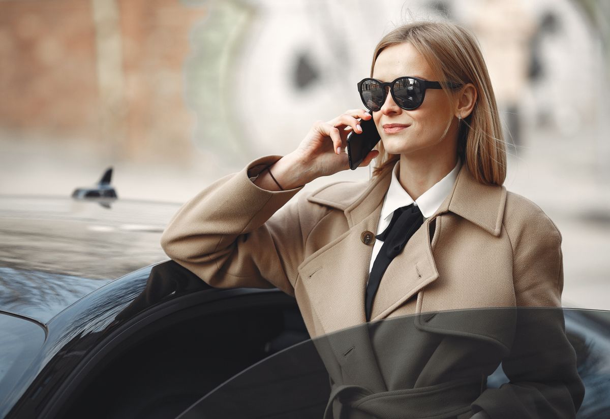Cliente, smartphone à l'oreille, à côté d'une voiture