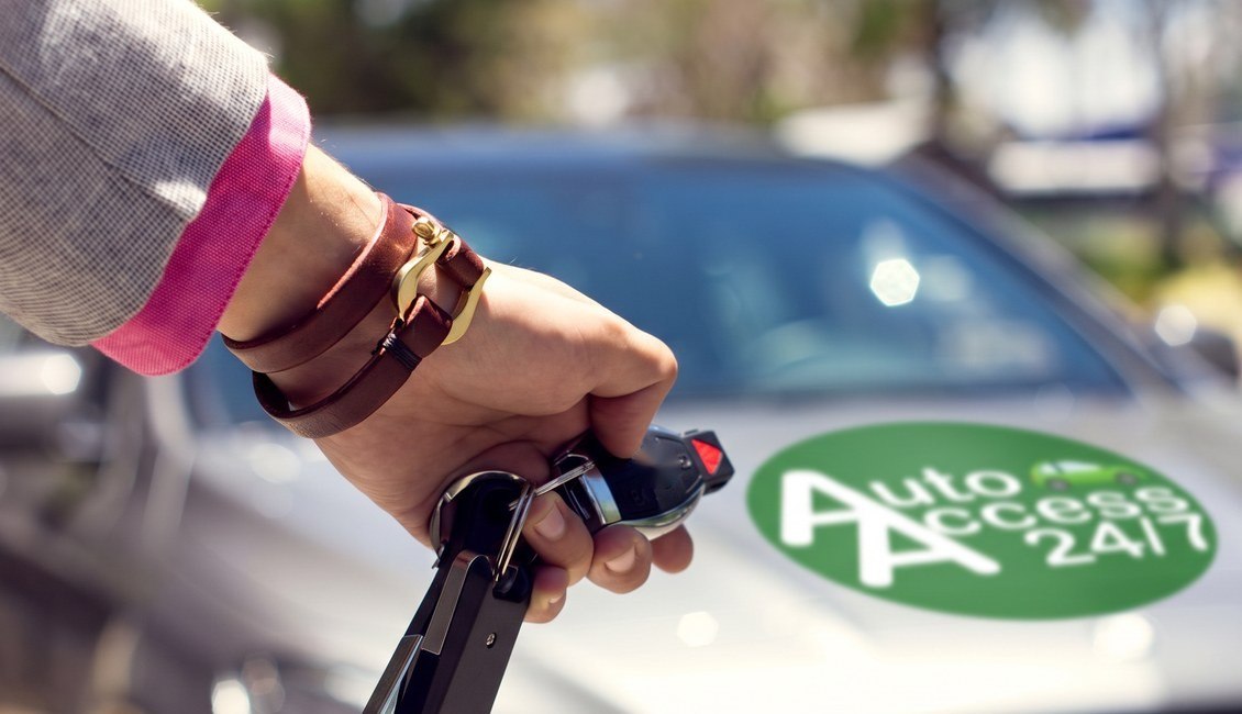 Main tenant des clés de voiture devant un véhicule au logo AutoAccess, prêt à être mis en location